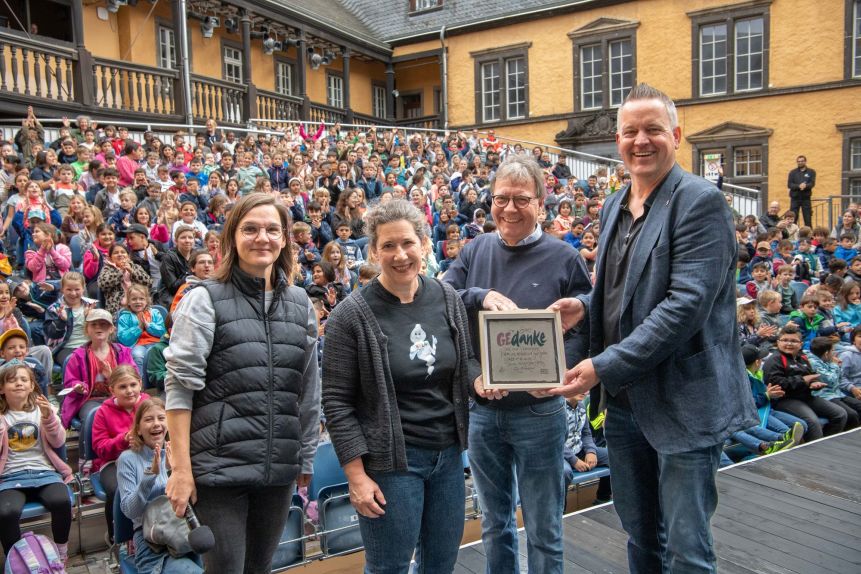 Die Kinder der flutgeschädigten Grundschule Bad Neuenahr auf den Zuschauerrängen der Burgfestspiele Mayen. Im Vordergrund vier Personen (Judith Kriebel(Dramaturgin), Ursula Bell (Rektorin), Heinz-P. Haupt (VP LC Mayen) und Carsten Strebel (Präsident LC Mayen)).